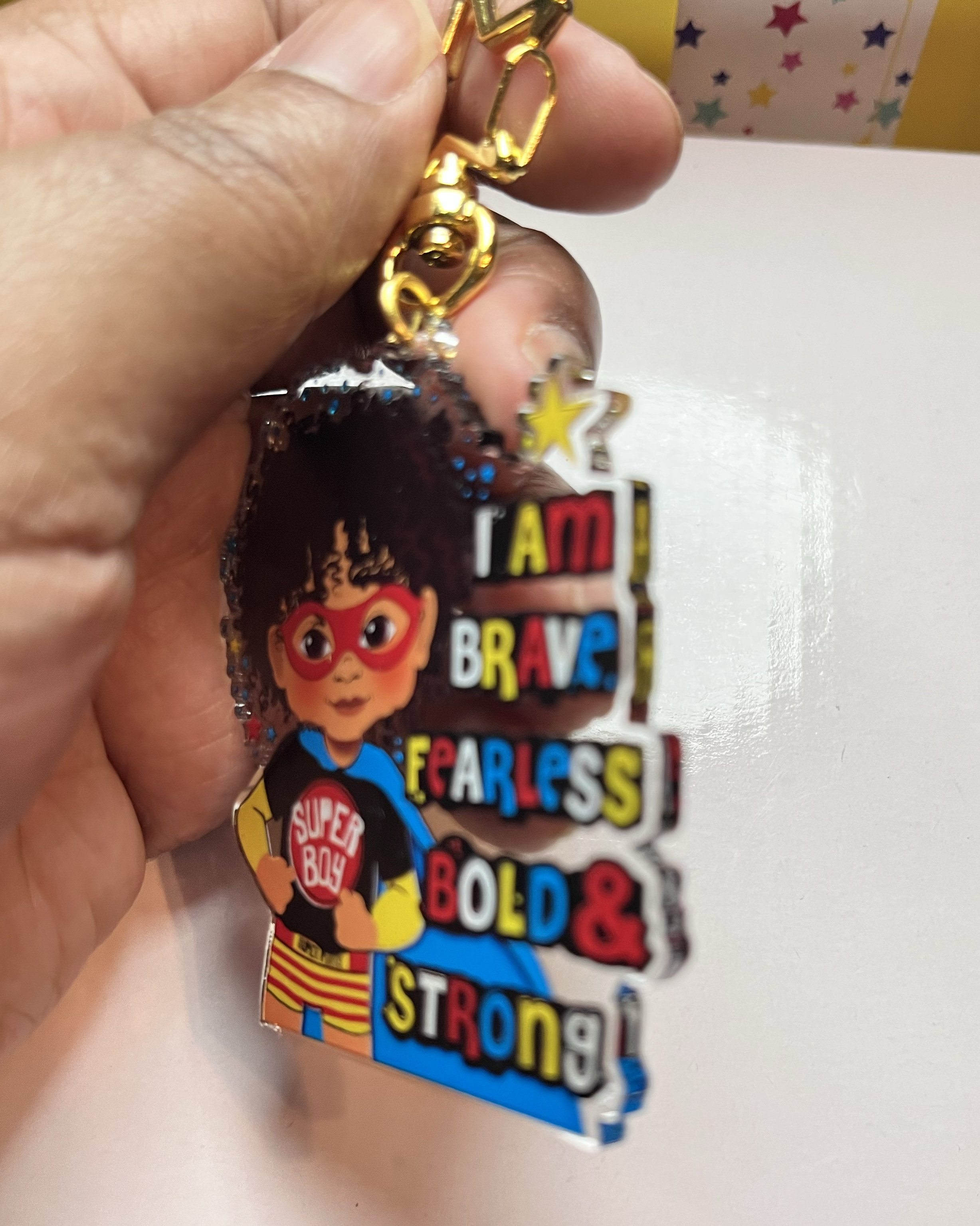 Side view colourful keychain with superhero design and motivational text held by a hand.