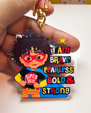 Keychain with brown boy superhero design and motivational text held by a hand.