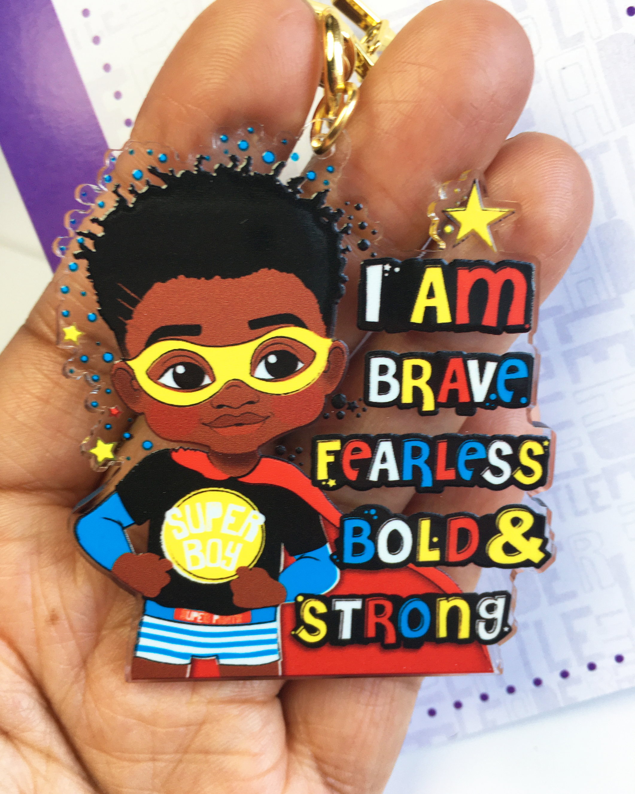 Affirmation keychain with a superhero-themed character and motivational text held in a hand.