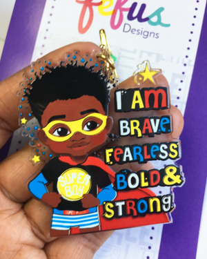 Black boy superhero design keyring featuring a confident child with curly hair and a cape by Fefus Designs. Text 'I am brave, fearless, bold & strong' held by a hand.