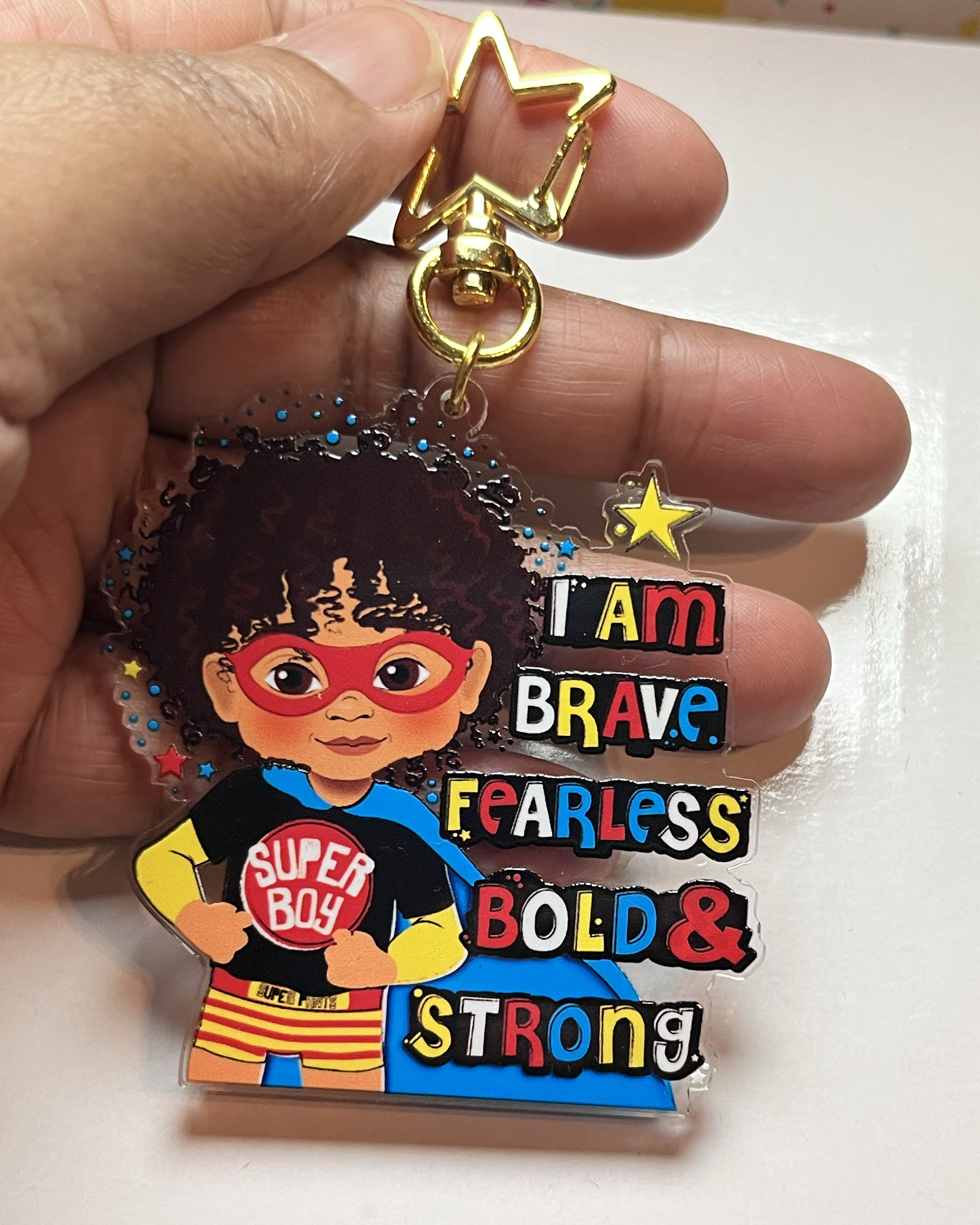 Keychain with mixed race superhero design and motivational text held by a hand.
