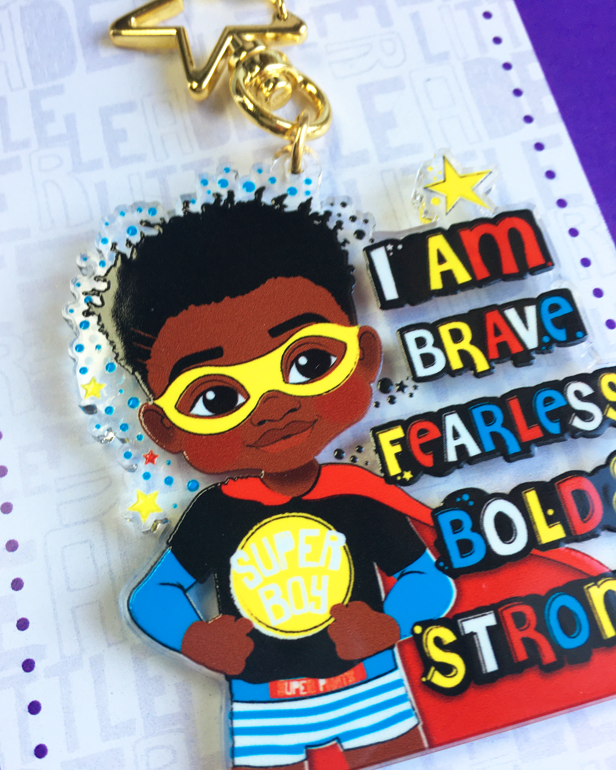Keychain with a black boy superhero-themed character and motivational text on a multicoloured background