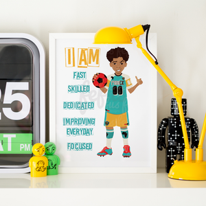 A framed personalized sports poster featuring a cartoon soccer player with the text 'I AM FAST SKILLED DEDICATED IMPROVING EVERYDAY FOCUSED' on a white background, styled on a shelf next to a yellow desk lamp, a digital clock, and small toy figures.