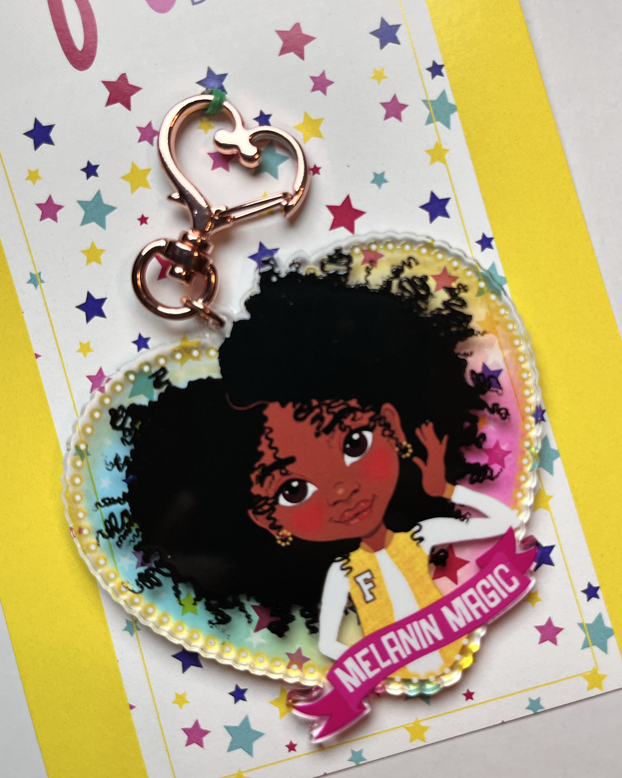 Keychain with illustration of a black girl with an afro set on a rainbow transparent background. Item comes mounted on a colourful star-patterned backing card.